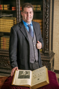 Professor Andrew Rabin in UofL's Ekstrom Library, standing next to an original copy of Shakespeare's Fourth Folio.