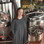 Becky Steele stands in front of equipment at False Idols Brewery.