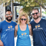 Three people, Dillon Miles, Danielle Huenefeld and Andy Huenefeld, standing together wearing sunglasses during a walking tour of Louisville.