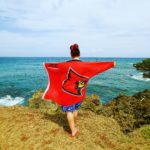 Cheyenne Hill holds a UofL flag overlooking a beach in Trinidad and Tobago.