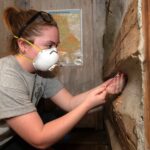 a student in a protective mask uses a wooden drill bit to extract a piece of wood from a cabin-like structure