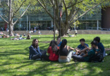 Students with backpacks laughing and sitting outside at UofL's Belknap Campus.