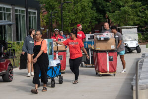 Students and volunteers move boxes and rolly carts into a residence hall on UofL's campus.