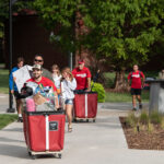 Students and families pushing red carts with their belongings.