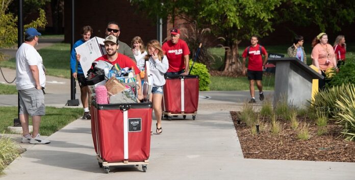 Students and families pushing red carts with their belongings.