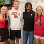 Four students stand in a line smiling