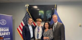 Congressman Morgan McGarvey, Jackson Robbins and Robbins' parents smile for a picture beside a United States flag and a Kentucky state flag.