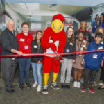 a group of adults, children and a mascot cut a ribbon