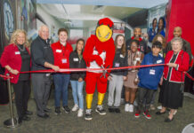 a group of adults, children and a mascot cut a ribbon