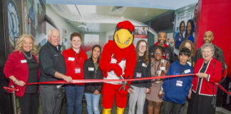 a group of adults, children and a mascot cut a ribbon