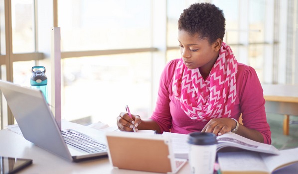 Person studying with a book in front of a computere.