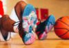 UofL Athletics Louie shoes close up with an image of Louie dunking a basketball. Basketball player wearing the shoes is sitting in the background with a basketball propped against their feet.