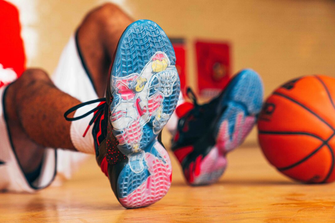 UofL Athletics Louie shoes close up with an image of Louie dunking a basketball. Basketball player wearing the shoes is sitting in the background with a basketball propped against their feet.