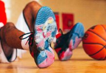 UofL Athletics Louie shoes close up with an image of Louie dunking a basketball. Basketball player wearing the shoes is sitting in the background with a basketball propped against their feet.