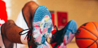 UofL Athletics Louie shoes close up with an image of Louie dunking a basketball. Basketball player wearing the shoes is sitting in the background with a basketball propped against their feet.